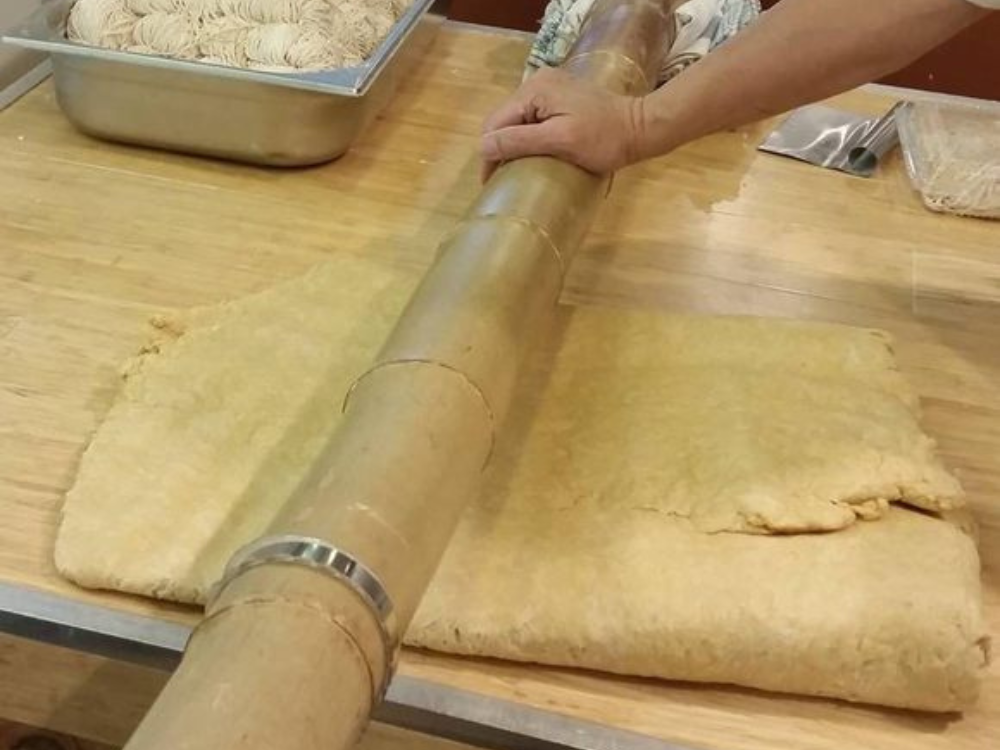 Workers hand-stretching mee suah dough on bamboo poles inside the LJMX factory